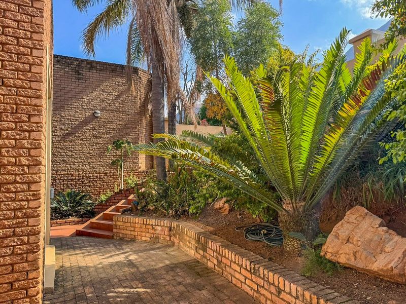 A landscaped garden area featuring a brick paved pathway, tiered brick retaining walls, a brick staircase, and established mature plantings.