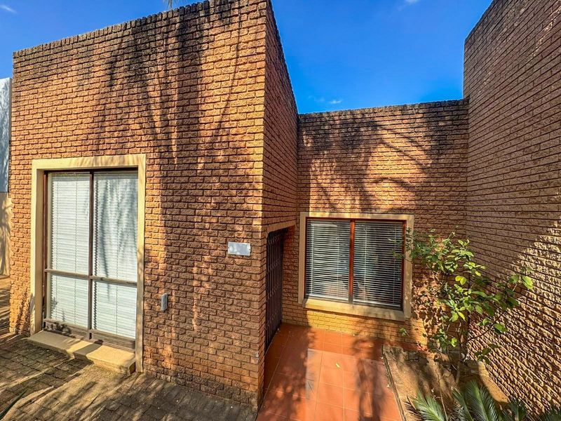 Front facade of a face brick house featuring a tiled entrance porch, security gate, and sliding glass door access.