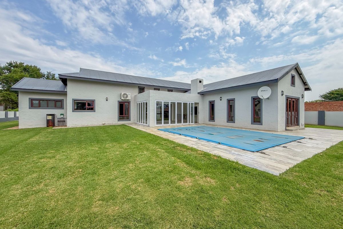 Rear view of the property featuring a swimming pool with a cover, a tiled patio area, and a well-maintained lawn.