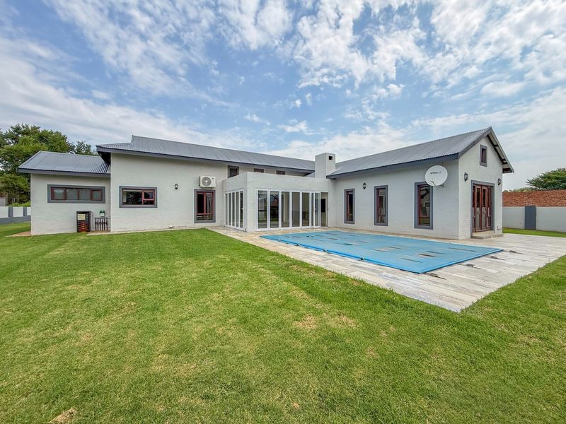 Rear view of the property featuring a swimming pool with a cover, a tiled patio area, and a well-maintained lawn.