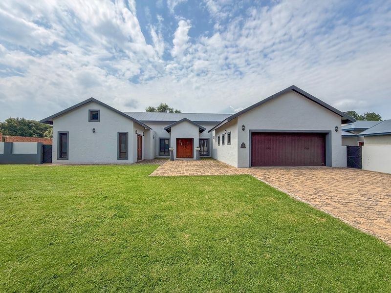 A well-maintained single-story residential property featuring a paved driveway, double garage, and a manicured front lawn with a prominent timber entrance.