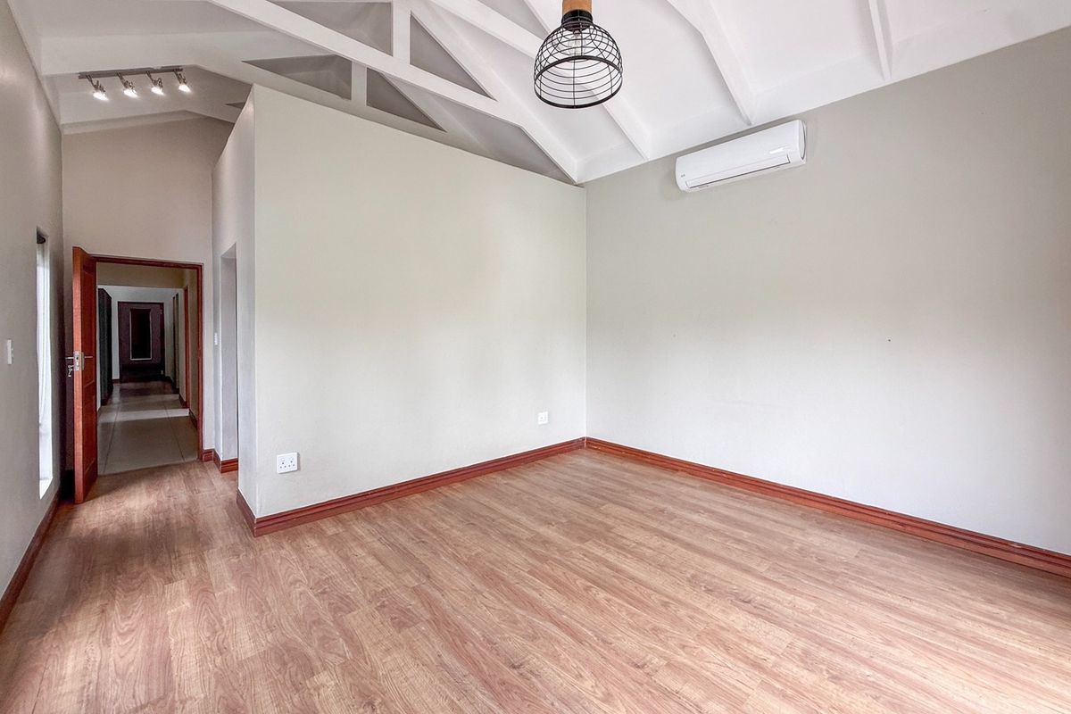 A bright, empty bedroom featuring vaulted ceilings with exposed trusses, laminate flooring, and a wall-mounted air conditioning unit.