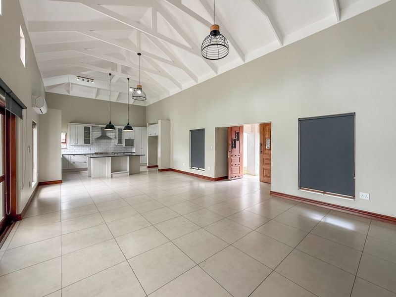 Spacious open-plan living and kitchen area featuring high vaulted ceilings with exposed trusses, modern cabinetry, a central island, and neutral tiled flooring.