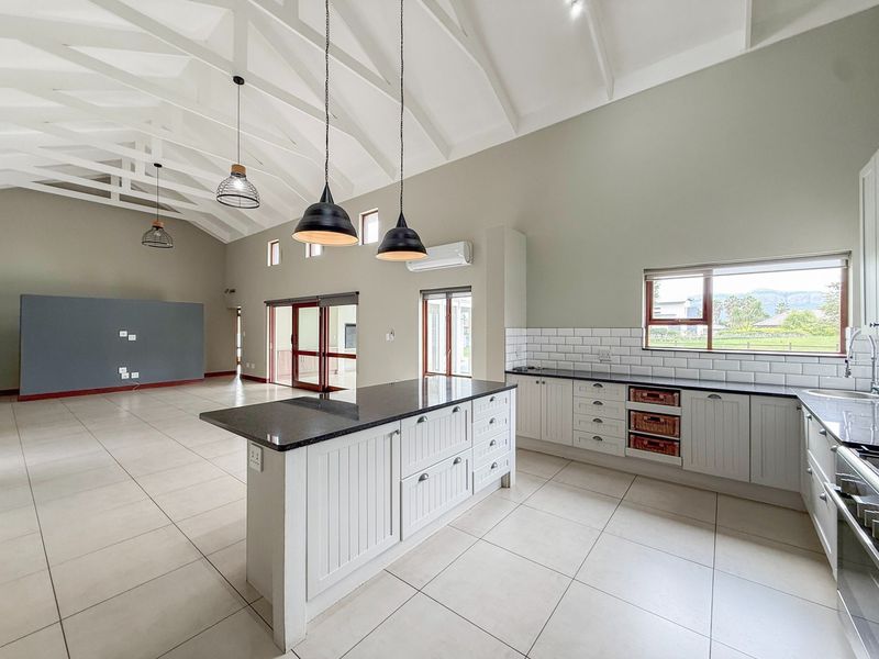 Spacious open-plan living and kitchen area featuring a high vaulted ceiling with exposed trusses, a central island, and modern tiled flooring throughout.