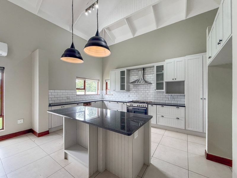 Modern kitchen featuring a central island, granite countertops, subway tile backsplash, gas stove with extractor, and high vaulted ceilings with pendant lighting.