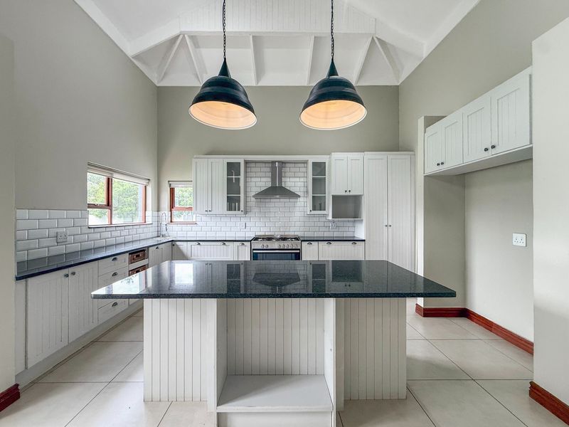 Spacious kitchen featuring a central island, granite countertops, subway tile backsplash, and a high vaulted ceiling with pendant lighting.