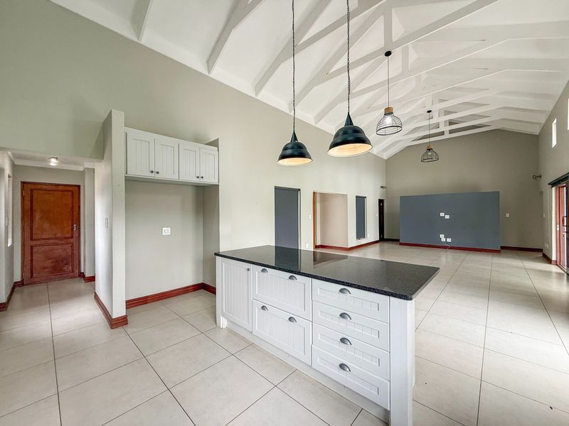 Spacious open-plan living area featuring a kitchen island with granite countertops, vaulted ceilings with exposed trusses, and neutral tiled flooring throughout.