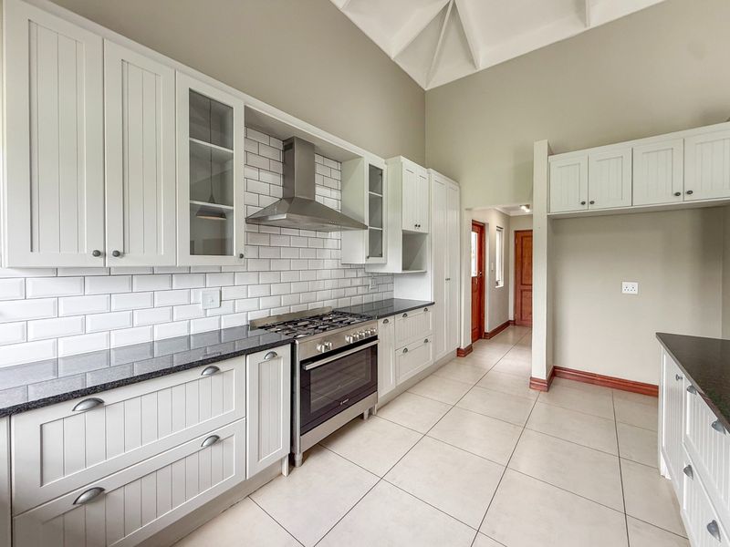 A bright, modern kitchen featuring white shaker-style cabinetry, granite countertops, a subway tile backsplash, and a stainless steel gas stove under a vaulted ceiling.