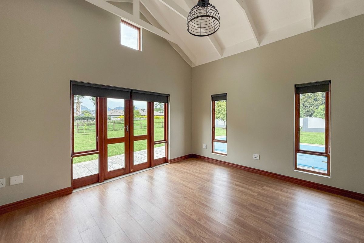 Spacious living area featuring vaulted ceilings with exposed rafters, laminate flooring, and large timber-framed glass doors providing access to the garden and pool area.