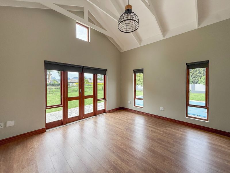 Spacious living area featuring vaulted ceilings with exposed rafters, laminate flooring, and large timber-framed glass doors providing access to the garden and pool area.
