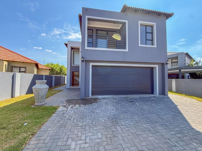 Modern double-storey residential property featuring a paved driveway, integrated double garage, and an upper-level balcony with contemporary grey facade finishes.