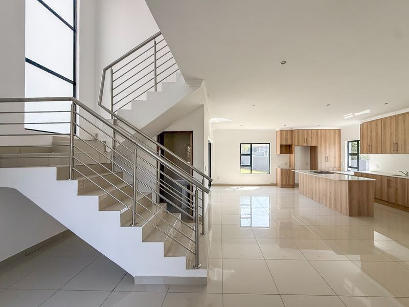 Spacious open-plan living area featuring a modern kitchen with wood-finish cabinetry, a central island, and a striking staircase with stainless steel railings.