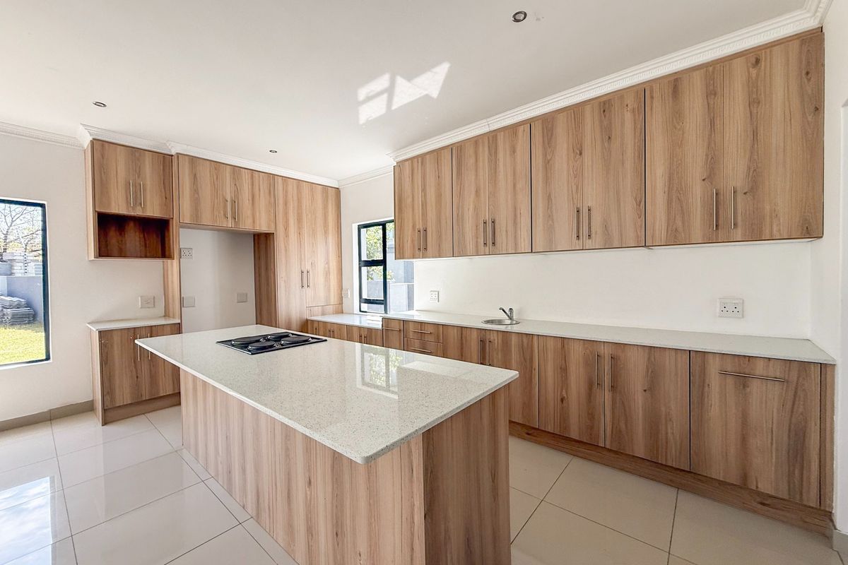 Modern kitchen featuring light wood-grain cabinetry, stone countertops, a central island with a built-in hob, and tiled flooring.