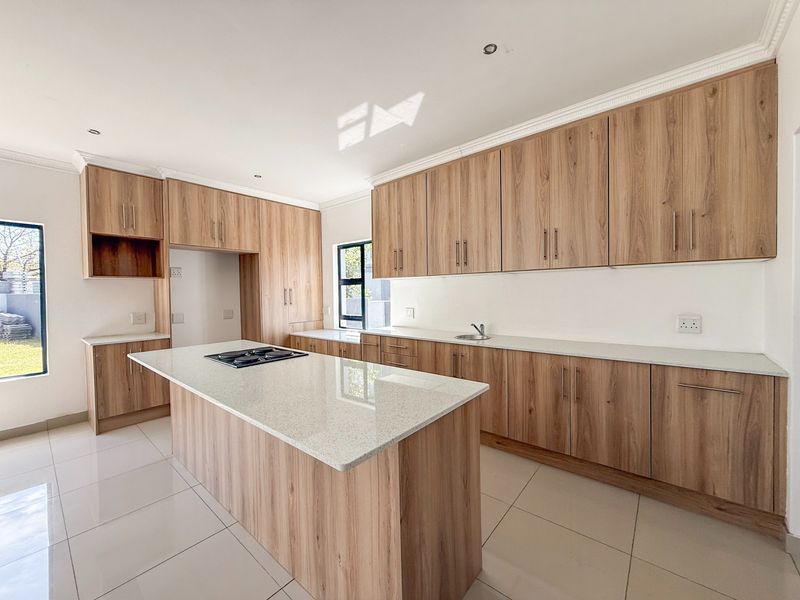 Modern kitchen featuring light wood-grain cabinetry, stone countertops, a central island with a built-in hob, and tiled flooring.