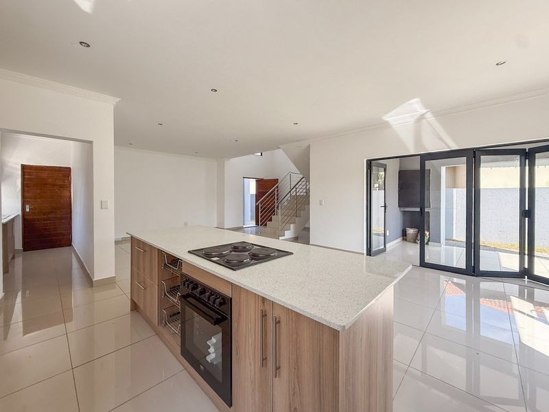 Spacious open-plan kitchen and living area featuring a central island with built-in oven, sleek tiled flooring, and large bi-fold doors leading to the patio.