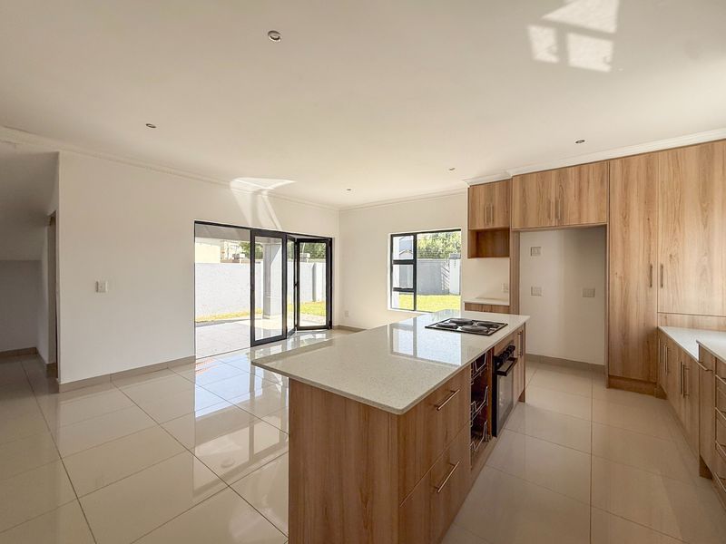Modern open-plan kitchen and living area featuring light wood cabinetry, stone countertops, a central island with a hob, and bi-fold doors leading to the garden.