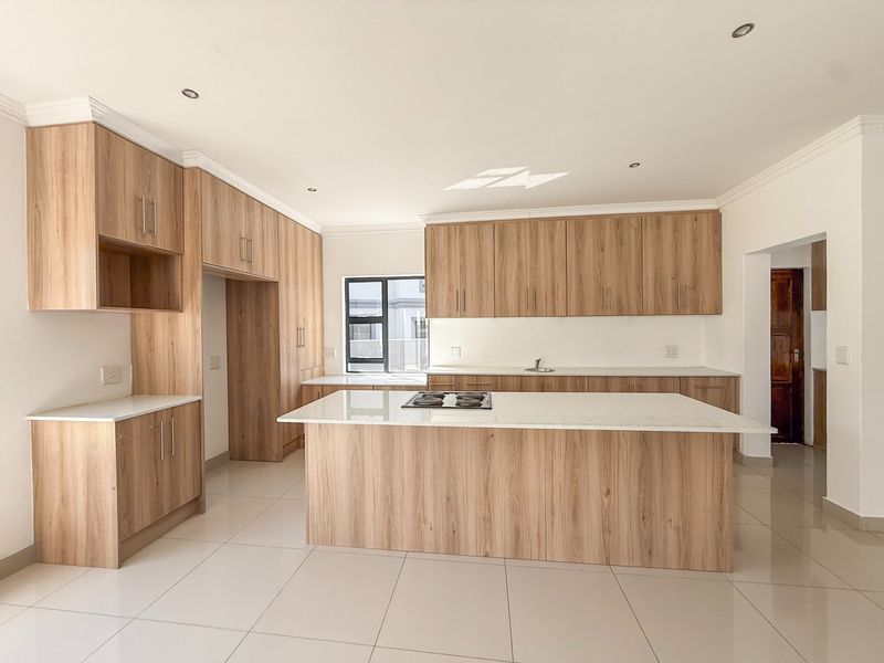 Modern kitchen featuring light wood-grain cabinetry, stone countertops, a central island with a gas hob, and tiled flooring.