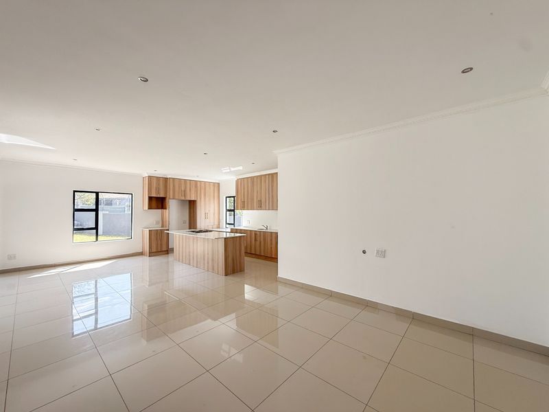 Spacious open-plan living and kitchen area featuring modern wood-finish cabinetry, a central island with a cooktop, and polished tiled flooring throughout.