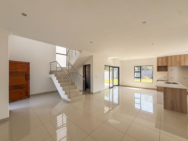 Spacious open-plan living area featuring modern tiled floors, a contemporary staircase, and a sleek kitchen with built-in cabinetry and island, leading to the garden.