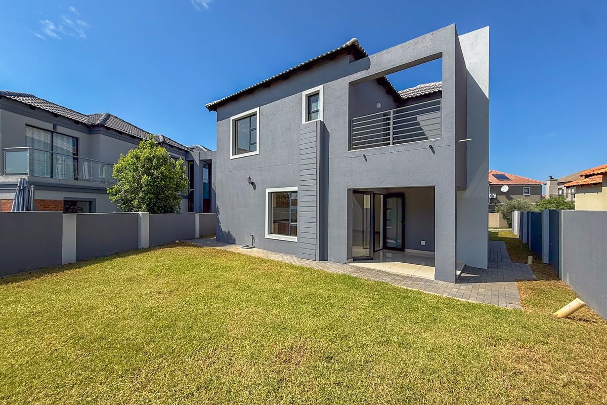 Rear view of a modern double-story house featuring a paved patio, balcony with metal railing, and a well-maintained private garden.