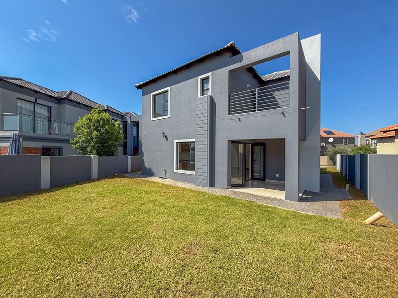 Rear view of a modern double-story house featuring a paved patio, balcony with metal railing, and a well-maintained private garden.