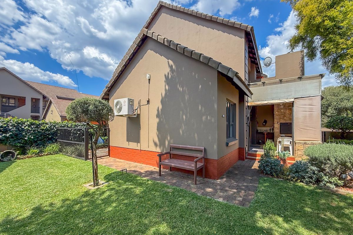 Rear view of the townhouse featuring a private garden, paved patio area, and a built-in braai under a covered section.