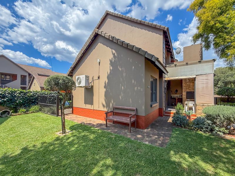 Rear view of the townhouse featuring a private garden, paved patio area, and a built-in braai under a covered section.