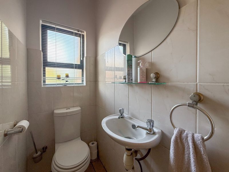 A compact guest bathroom featuring tiled walls, a wall-mounted basin, and a toilet, providing a functional and clean space.