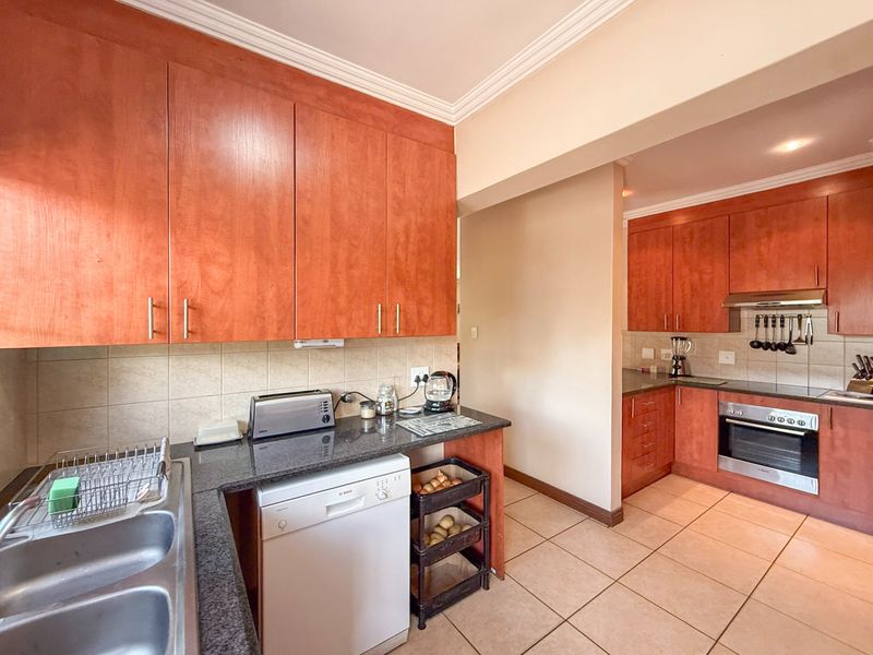 A functional kitchen featuring warm-toned wooden cabinetry, granite countertops, tiled flooring, and integrated appliances including an oven and extractor fan.