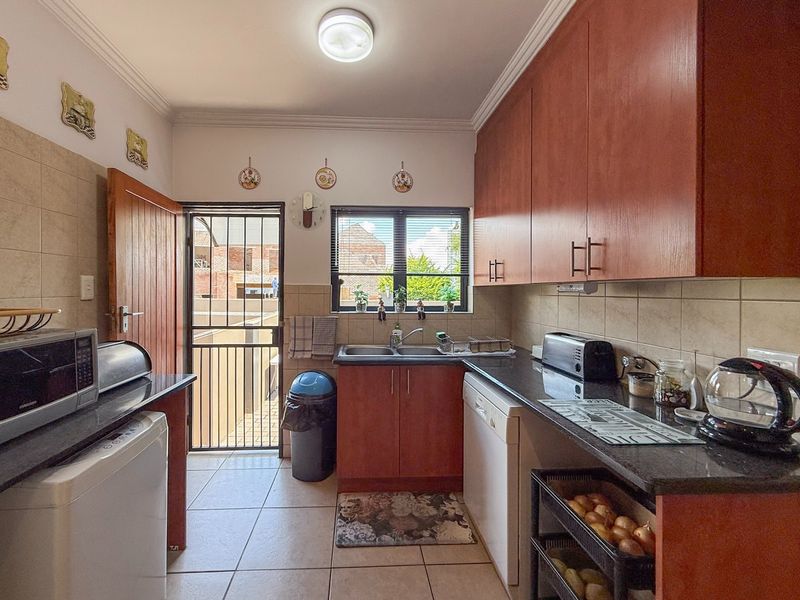Functional kitchen featuring laminate cabinetry, granite countertops, double basin sink, and tiled flooring with direct access to an exterior security gate.
