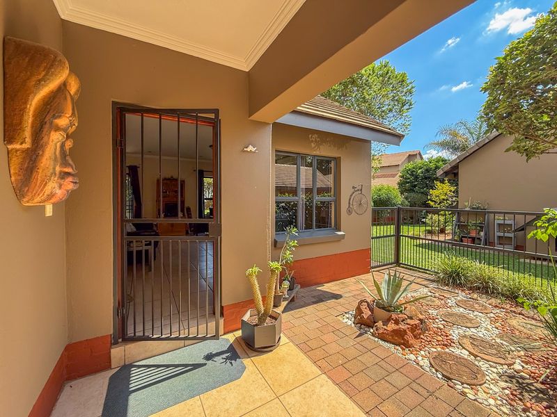 A covered patio area featuring tiled flooring, a security gate entrance, and a paved garden section with metal perimeter fencing.