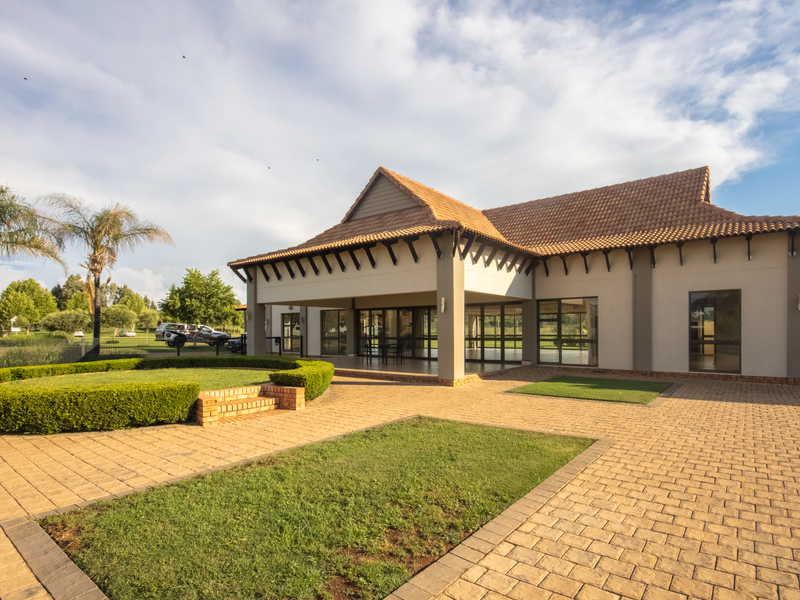 A well-maintained rear exterior view featuring a spacious paved courtyard, landscaped garden beds, and a covered patio area with large glass sliding doors.