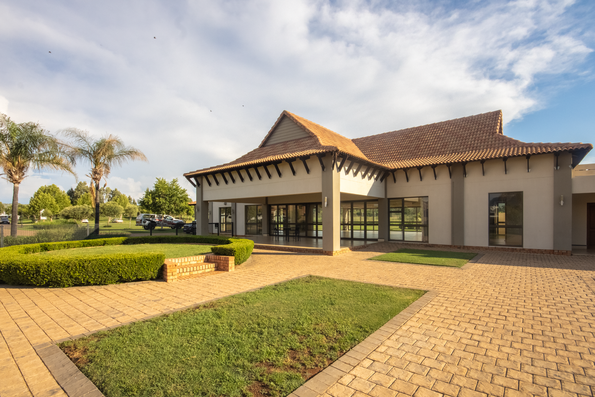 A well-maintained rear exterior view featuring a spacious paved courtyard, landscaped garden beds, and a covered patio area with large glass sliding doors.