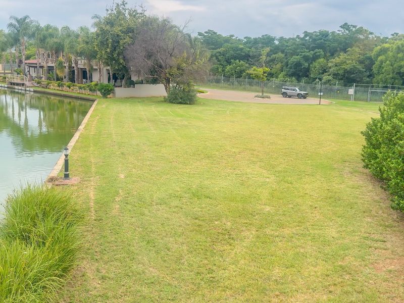A well-maintained waterfront garden area featuring a manicured lawn, established landscaping, and direct access to the water's edge.