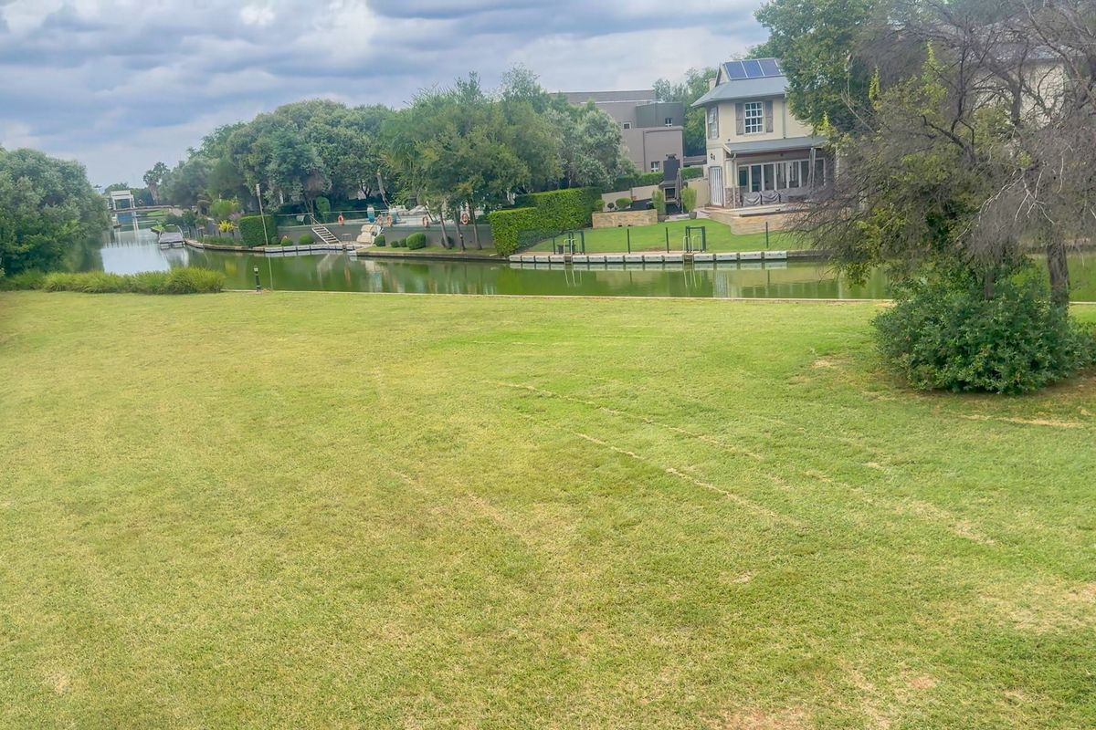 A scenic view of a residential waterfront property featuring a large, well-maintained lawn and canal access.