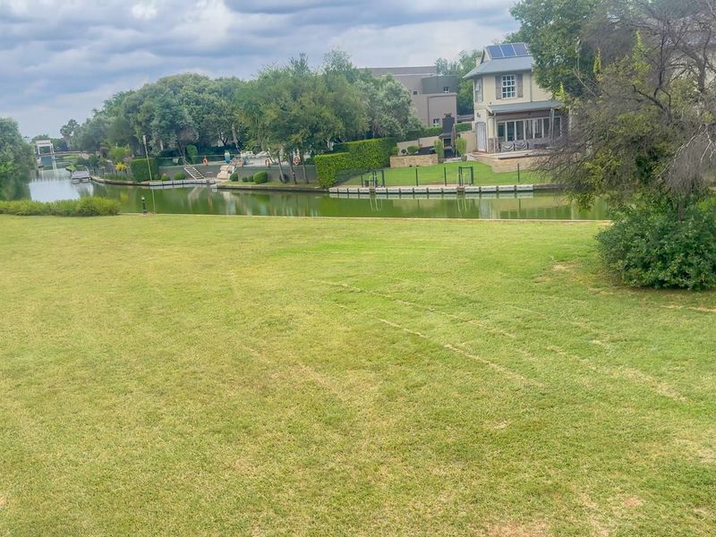 A scenic view of a residential waterfront property featuring a large, well-maintained lawn and canal access.