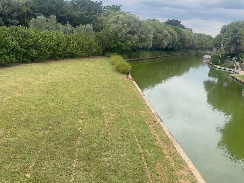 A scenic view of a residential waterfront canal bordering a well-maintained grass lawn and mature trees.