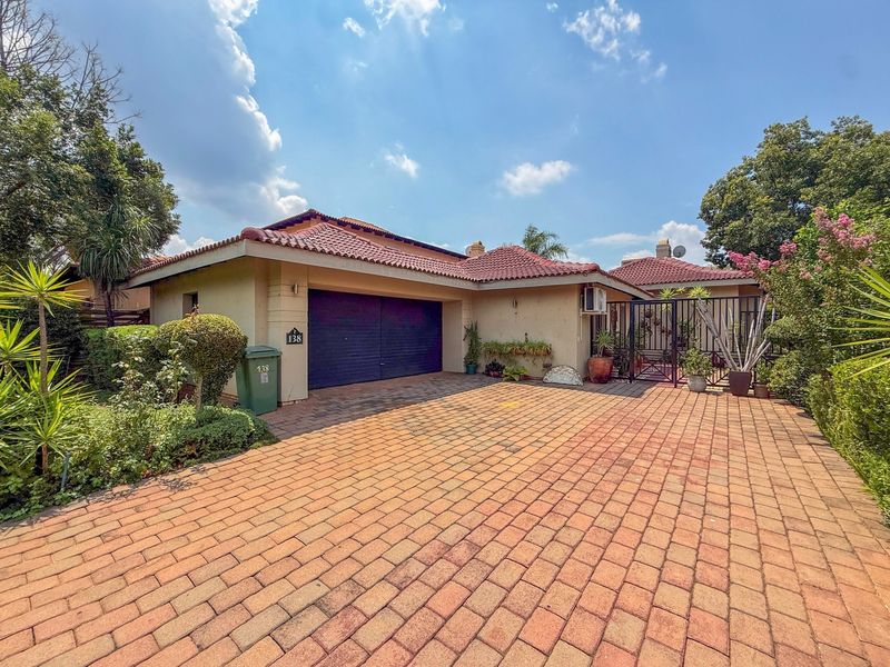 Front view of a single-story house featuring a paved driveway, double garage, and tiled roof with established garden surroundings.