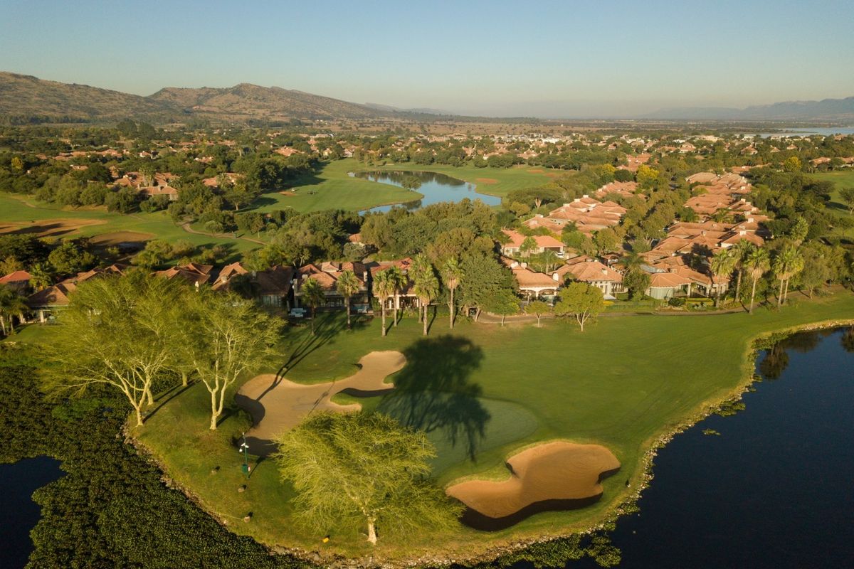 An aerial view of a residential estate situated alongside a golf course, featuring manicured greens, water hazards, and surrounding landscape.