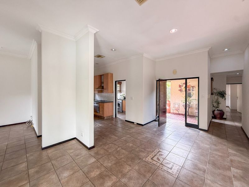 Spacious open-plan living area featuring tiled flooring, recessed lighting, and direct access to an outdoor patio, with an adjoining kitchen space.
