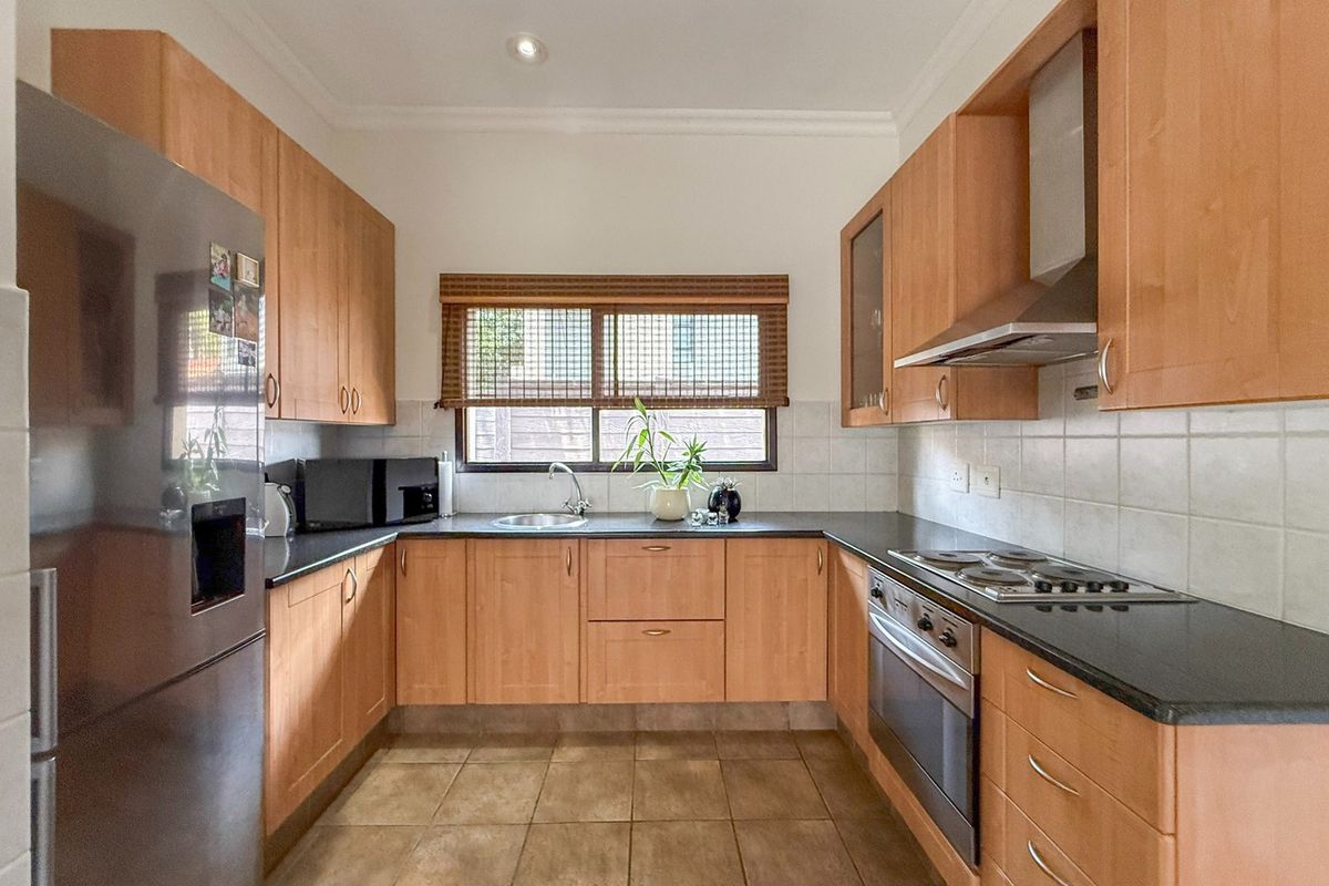 A functional kitchen featuring light wood cabinetry, dark countertops, integrated stainless steel appliances, and tiled flooring with a window overlooking the exterior.