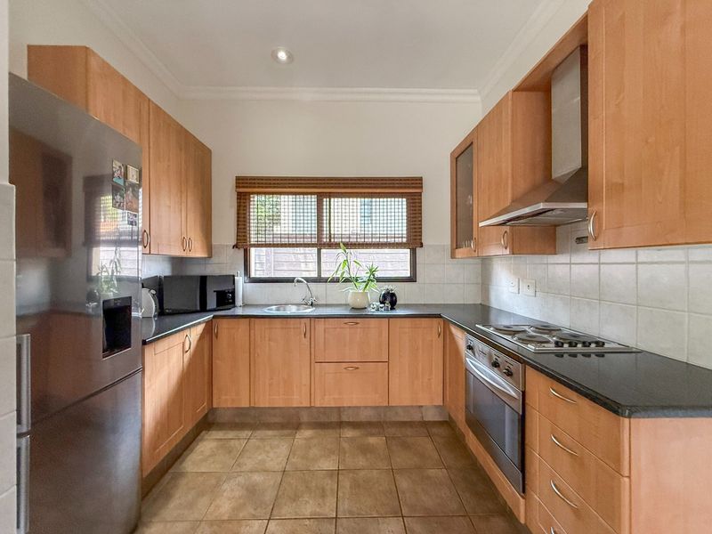 A functional kitchen featuring light wood cabinetry, dark countertops, integrated stainless steel appliances, and tiled flooring with a window overlooking the exterior.
