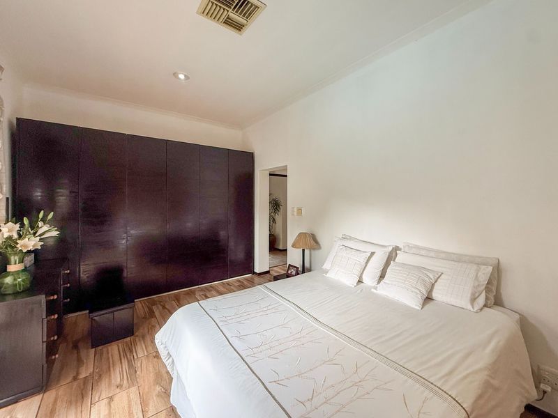 A well-maintained bedroom featuring dark built-in cupboards, wood-look tile flooring, and integrated ducted air conditioning.