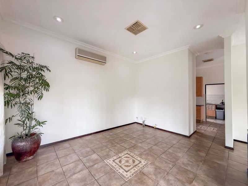 An empty living area featuring tiled flooring with a decorative inlay, recessed lighting, and a wall-mounted air conditioning unit, leading into a kitchen space.