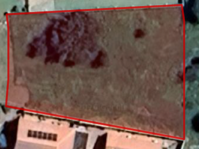 An aerial view of a vacant residential plot with a red boundary overlay indicating the property lines.