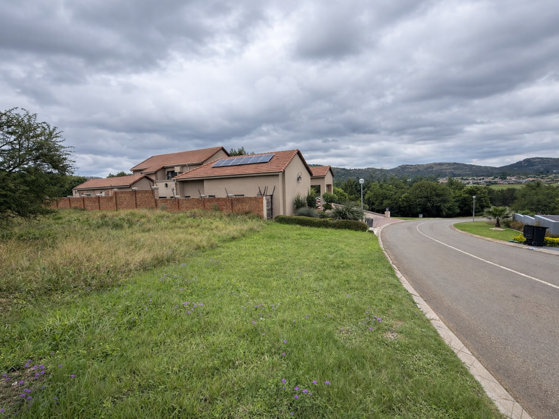 Street view of a residential property featuring a tiled roof with solar panels and a brick boundary wall, set in a landscaped estate.