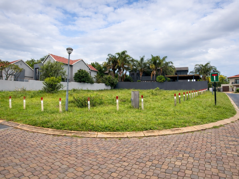 A vacant residential corner plot featuring established boundary walls, paved street access, and utility connections in a developed neighborhood.