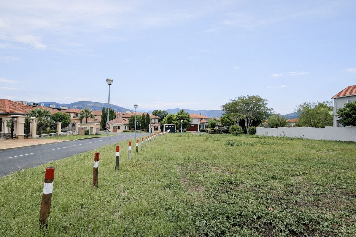 A vacant residential plot situated along a paved street in a developed estate, featuring established boundary walls and street lighting.