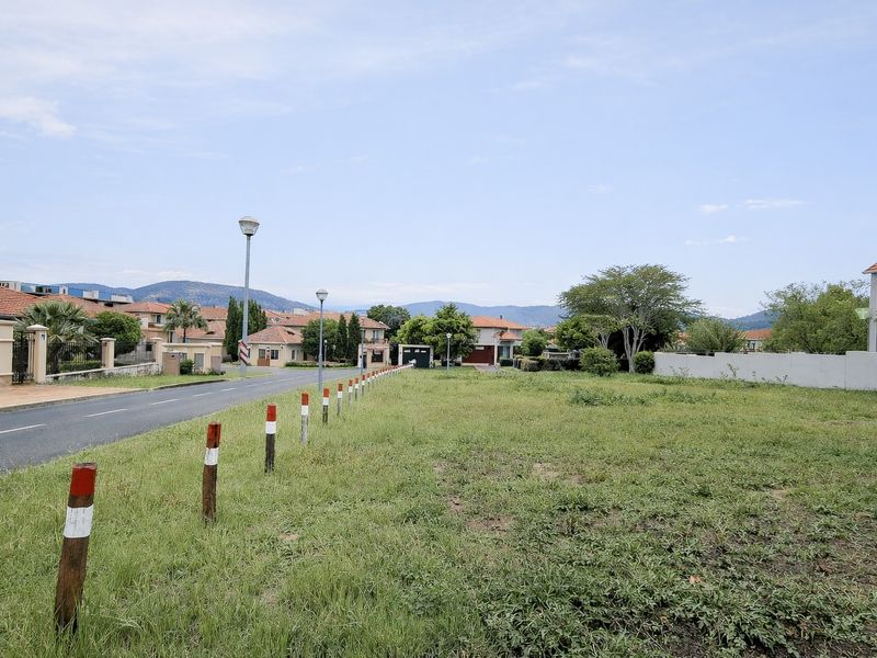 A vacant residential plot situated along a paved street in a developed estate, featuring established boundary walls and street lighting.