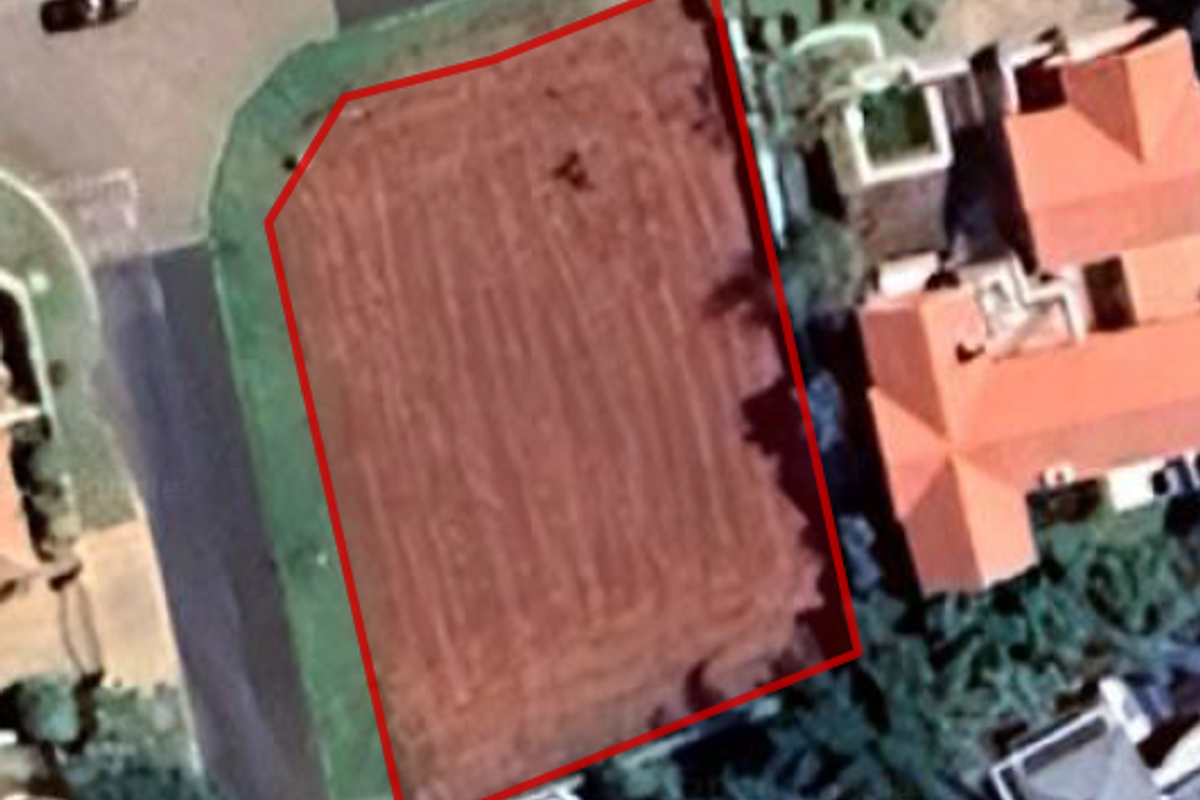 An aerial view of a vacant residential plot of land, clearly outlined in red, situated within a developed neighborhood.